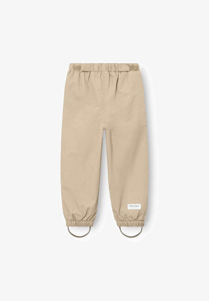 Beige wasserfeste Kinderhose mit elastischem Bund, gesammelten Bündchen, Fußriemen und einem kleinen weißen Logo-Patch am linken Bein.