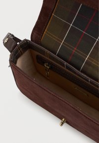 Brązowa torebka z zamszu z kratkowym wnętrzem. Posiada kieszeń na zamek błyskawiczny i zapięcie na klamrę. Teksturowana zewnętrzna strona i gładkie wykończenie wnętrza.