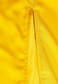 Tejido amarillo con una textura suave y satén, que presenta una abertura y detalles de costura precisos. Color brillante y superficie elegante.