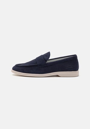 Mocasines de ante azul marino con punta redondeada y detalles de costura. Presentan una lengua acolchada y una suela de goma beige claro para mayor comodidad.