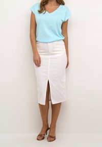 Maglietta azzurra chiaro a scollo a V e gonna in denim bianca al ginocchio con spacco frontale. Sandali beige con tacco e cinturini incrociati completano il look.