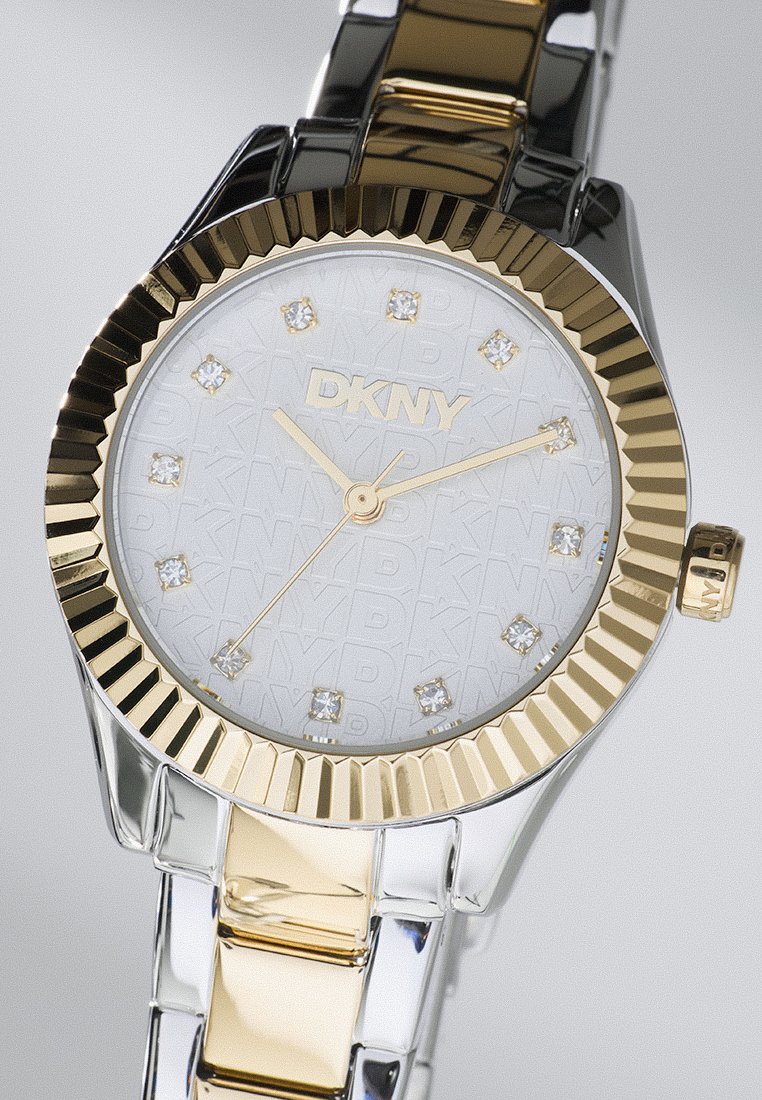 Orologio DKNY oro e argento con quadrante bianco testurizzato, caratterizzato da uno sfondo a fantasia e indici delle ore in cristallo. Bracciale a maglie metalliche.