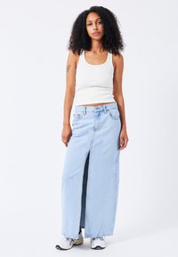 falda de mezclilla azul clara con una abertura frontal y un corte relajado, combinada con una camiseta sin mangas blanca de canalé y zapatillas blancas.