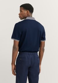 Polo shirt navy con colletto e polsini grigi a contrasto, maniche corte e vestibilità comoda, abbinato a pantaloni di lino scuri.