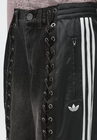 Μ αύρο παντελόνι με σχέδιο κορδονιών στις πλευρές, υφή γκρι τζιν, με λευκές ρίγες και τσέπη με φερμουάρ. Μετατρέψιμο στυλ.