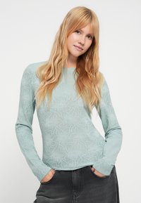 Ανοιχτό μέντα πράσινο πουλόβερ με μακριά μανίκια και ανάγλυφο ανθικό σχέδιο, στρογγυλή λαιμόκοψη και εφαρμοστή γραμμή. Συνδυασμένο με σκούρα γκρι τζιν.