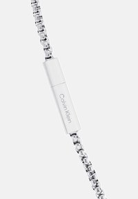 Sølv kædearmbånd med en elegant lås med "Calvin Klein" indgravering, der viser en poleret metalfinish og sammenkædede design.