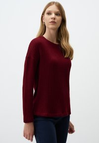 Bordeaux gebreide trui met een ronde hals, lange mouwen en een gestructureerd, ribbelontwerp. Gepaard met donkerblauwe broek.