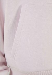 Sweat à capuche rose clair en matière douce, avec une poche avant et un ourlet côtelé. Design simple sans motifs ni accessoires visibles.