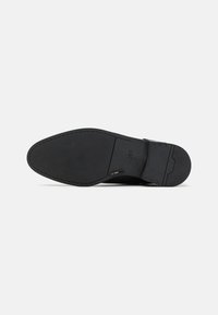 Black leather shoe sole with smooth texture, featuring a rectangular shape, shallow tread pattern, and subtle brand logo embossed.