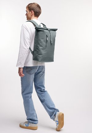 Grau Rolltop-Rucksack aus wasserdichtem Material, ausgestattet mit verstellbaren Trägern und einer vorderen Reißverschlusstasche. Glatte Textur, minimalistisches Design.