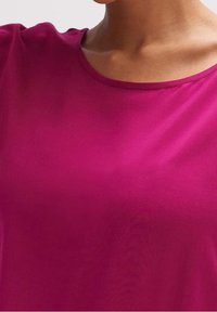 Fuchsiové tričko s krátkým rukávem a kulatým výstřihem, vyrobené z hladké, lehké tkaniny s jemným leskem. Jednoduchý, nezdobený design.