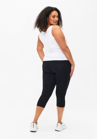 Black capri leggings with a smooth texture paired with a white sleeveless top. The outfit features a fitted design and classic colors.