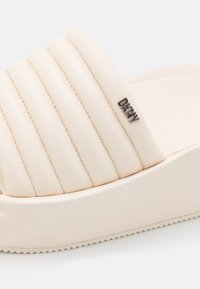 Sandale à glissière beige avec un design nervuré, en cuir lisse. Présente une pointe carrée et un accent logo subtil sur la lanière.