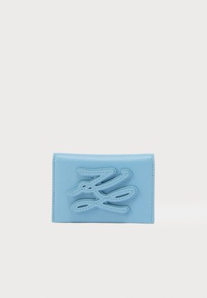 Portafoglio in pelle azzurro chiaro con un design testurizzato e cucito. Presenta un logo astratto prominente sulla parte anteriore e una finitura liscia.