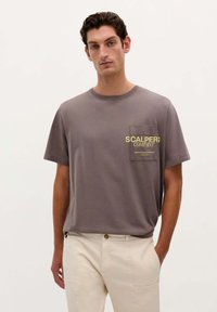 Grå bomulds t-shirt med korte �ærmer, rund halsudskæring og en brystlomme med gul "SCALPERS COMPANY" tekst.