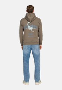 Sudadera gris con un gráfico de escorpión en la espalda, combinada con jeans ajustados de color azul claro y zapatillas blancas. Material de algodón, corte relajado.