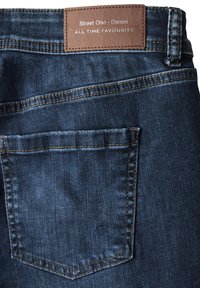 Mörkblå denimjeans med kontrasterande gyllene sömmar, med en bakficka och en brun läderetikett som säger "Street One - Denim."