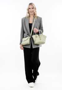 Blazer grigio su top nero, abbinato a pantaloni neri a gamba larga. Borse in pelle verde chiaro: una strutturata e una a tracolla con pattina.