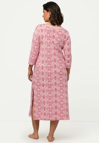 Dlouhý růžový župan s květinovým vzorem, tříčtvrtečními rukávy, bočními rozparky a volným střihem, vyrobený z měkké tkaniny.