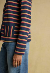 Námornícky a pruhovaný kardigán s vodorovnými pruhmi v ružovej a béžovej farbe, s vreckom a výšivkou "JOULES" na rukáve.