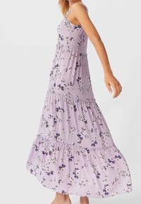 Maxi-jurk van licht lavendelkleurige stof, met bloemenpatronen, spaghettibandjes en tiered ruches aan de zoom. Zorgt voor een soepele textuur.