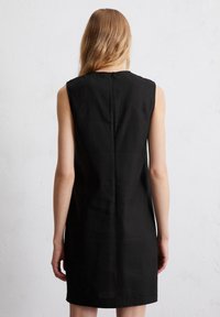 Schwarzes ärmelloses Kleid mit einem hohen Kragen, taillierter Form und einer zentralen Naht auf der Rückseite. Hergestellt aus glattem Stoff.
