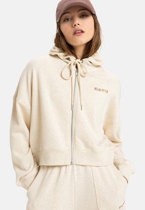 Beige cropped hoodie with a drawstring hood and front zip closure. Features soft texture and a small "Roxy" logo in a contrasting color.