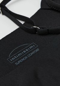 Svart plagg med en slät textur, med justerbara remmar och en synlig logotyp märkt "intimissimi SUPERIOR COMFORT."
