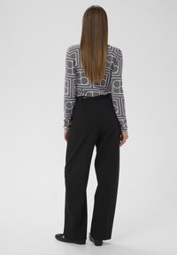 Langærmet top med et gråt geometrisk mønster, kombineret med højttaljede sorte bukser med vide ben og sorte flade sko.