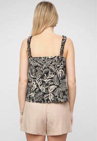 Top in tessuto nero con motivo floreale, dotato di spalline arricciate e disegno a foglie beige. Abbinato a pantaloni corti beige chiaro, che offrono una vestibilità comoda.
