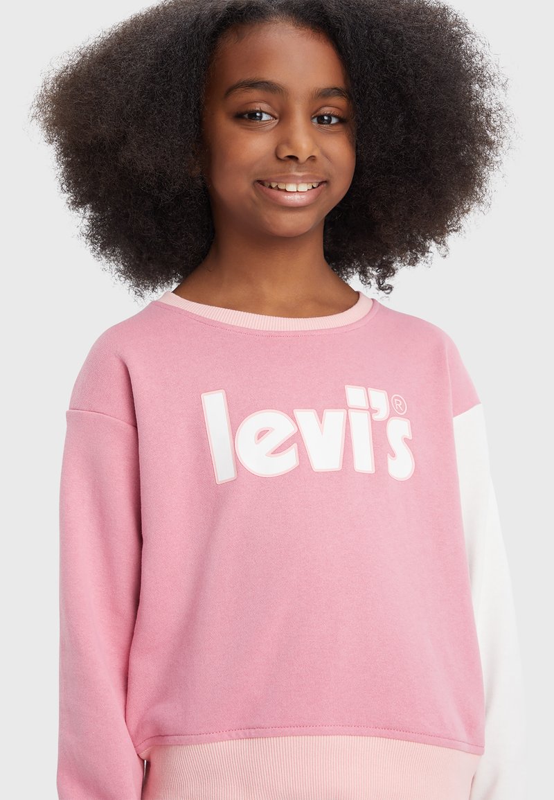 Sweatshirt rose clair avec des accents blancs et un grand logo "levi's". Il dispose d'un col rond et d'un ourlet côtelé, fabriqué dans un tissu doux et texturé.