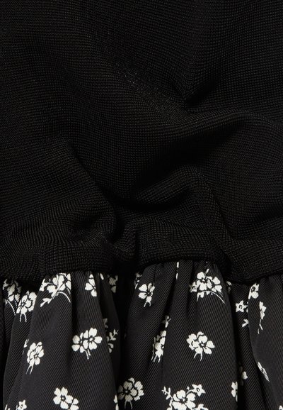 Tissu noir texturé en haut, se dégradant vers une jupe à fleurs noires et blanches à volants avec des rayures horizontales.