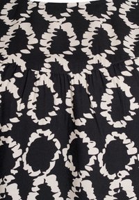 Tissu noir avec un grand motif floral abstrait blanc. Présente un détail froncé le long de la couture, ajoutant de la texture au design.