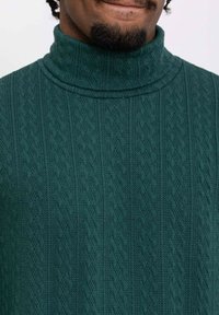 Pull en col roulé vert foncé en tissu tricoté, présentant un motif texturé avec des lignes verticales et un col côtelé.