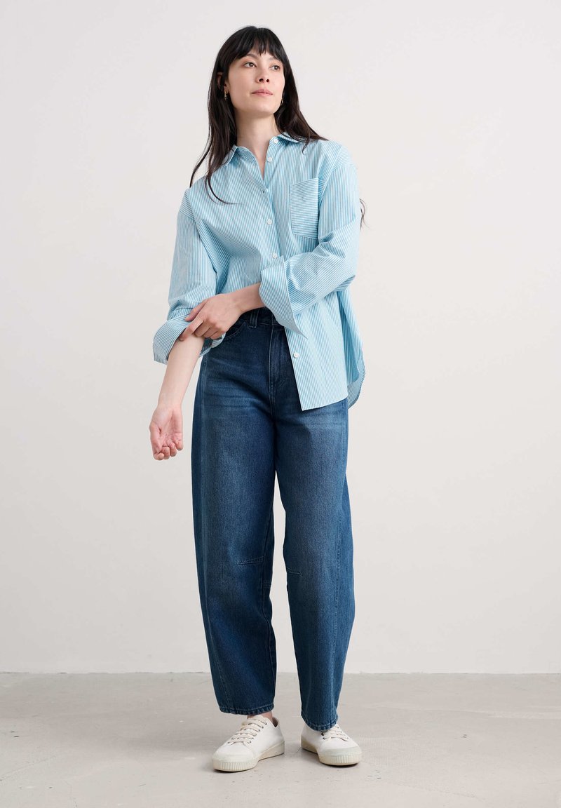 Lichtblauwe, gestreepte overhemden met een borstzak en opgerolde mouwen, gecombineerd met wijde, donkerblauwe jeans en witte sneakers.