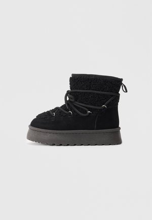Botte d'hiver noire avec une semelle à épaisseur épaisse, un collier supérieur en polaire et un détail de lacet enroulé sur fond blanc.