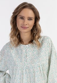 Világoskék mintás ruha virágos mintákkal, gombos elejével, kerek nyakkivágással és gyűrt derékkal. Puha, áramló szövettextúra.
