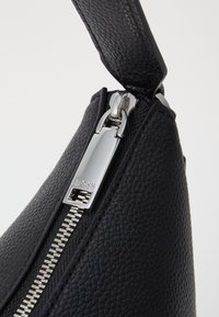 Musta nahkainen käsilaukku tekstuuripinnalla, jossa on hopeinen vetoketju ja "BOSS"-merkitty vetotappi. Suunnittelu on tyylikäs ja moderni.