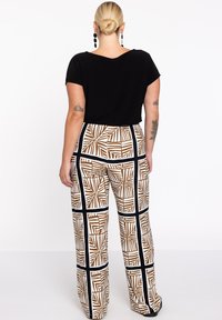 Schwarzes kurzärmliges Oberteil, kombiniert mit einer weit geschnittenen Hose, die ein geometrisches Braun- und Weißmuster aufweist, umrandet von schwarzen Akzenten.