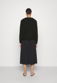 Czarny sweter z okrągłym dekoltem i długimi rękawami, zestawiony z ciemną plisowaną spódnicą midi. Całość dopełniają beżowe sandały na płaskiej podeszwie.