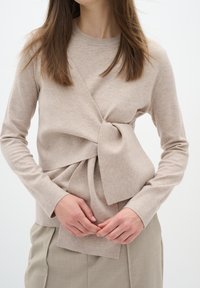Beige gestrickter Pullover mit einem verdrehten Vorderdesign und Schleifendetail. Lange Ärmel und runder Halsausschnitt. Weicher Stoff und figurnahe Silhouette.