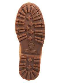 Semelle en caoutchouc tan avec des motifs de traction profonds et des détails en forme de croix. Logo Timberland embossé au centre au-dessus d'un design circulaire.