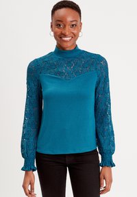 Top a maglia turchese con maniche lunghe in pizzo trasparente e scollatura alta, caratterizzato da un corpino aderente e polsini arricciati.