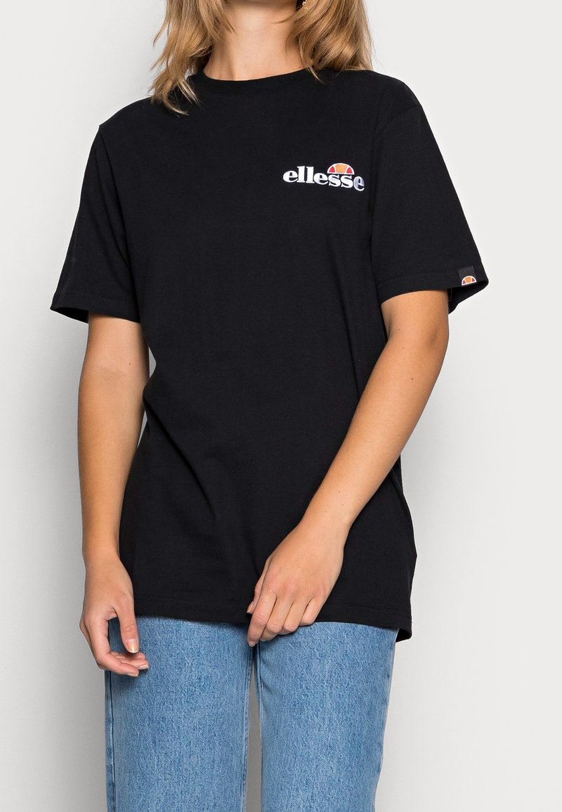 T-shirt noir en coton à manches courtes. Présente un logo blanc "ellesse" sur la poitrine et un accent coloré sur la manche.