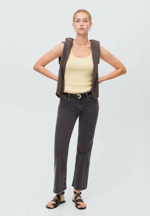 Jeans anchos grises, top de tirantes amarillo claro y un chaleco corto marrón. Sandalias planas negras con tiras cruzadas completan el atuendo.