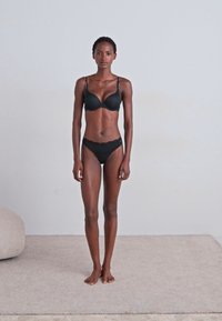 Crni set donjeg rublja koji uključuje podstavljenu bralette i odgovarajuće gaćice s bikini izrezom. Glatka tkanina s podesivim trakama i ukrasnim čipkastim obrubom.