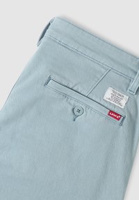 Φωτεινά γαλάζια παντελόνια Levi's με κουμπωτή πίσω τσέπη και κόκκινη ετικέτα Levi's με το λογότυπο κοντά στη ραφή της τσέπης.