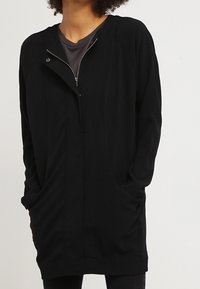 Svart zip-up ytterkläder gjorda av ett lätt material, med en avslappnad passform, två sidofickor och en hög krage.