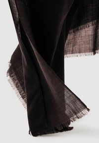 Material ușor de culoare maro închis, cu margini desfăcute, pliat liber și atârnând pe un fundal deschis.